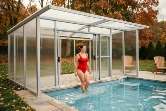 Femme entrant dans une piscine couverte par un abri polycarbonate en automne dans un jardin résidentiel