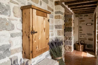 Meuble cache compteur électrique en bois brut fixé sur un mur en pierre dans un couloir de maison de campagne française